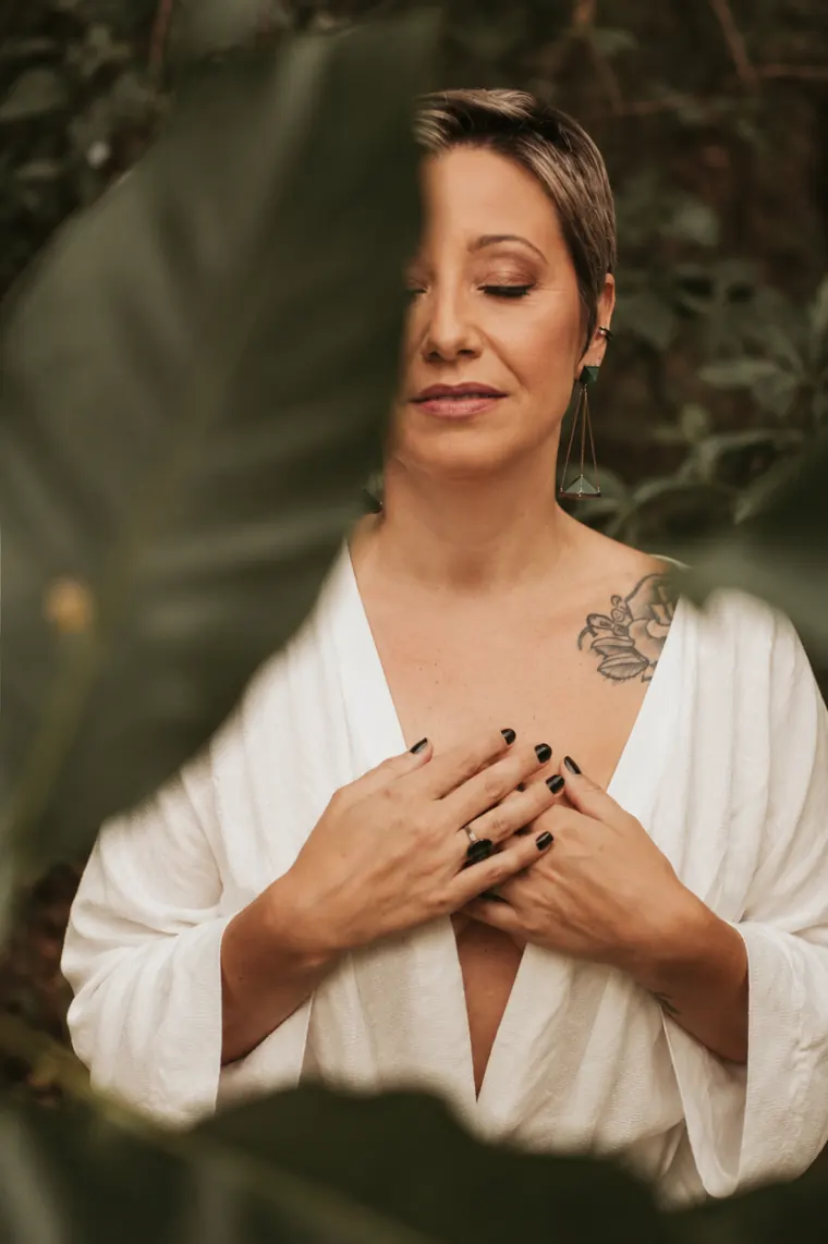 Tatti Santos de olhos fechados, com as mãos sobre o coração, entre folhas.